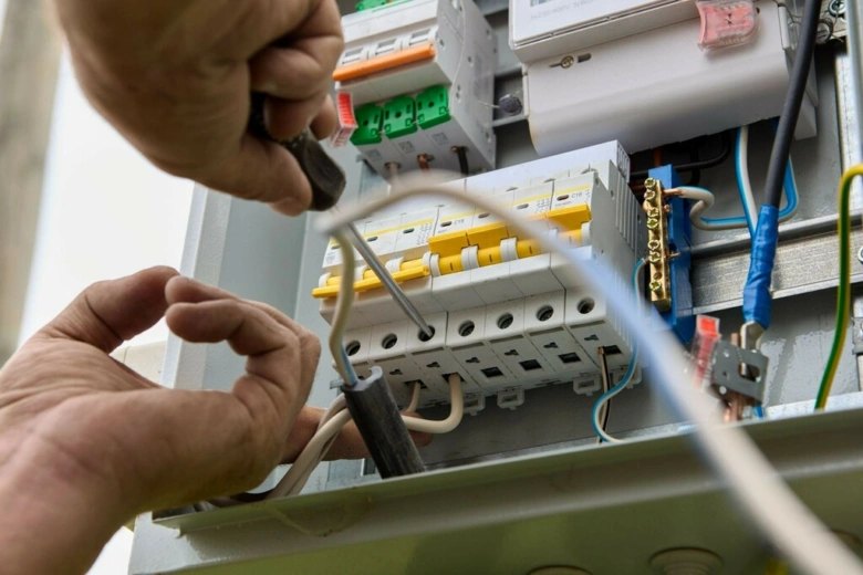 Elektrikář montuje jistič do rozvaděče šroubovákem.