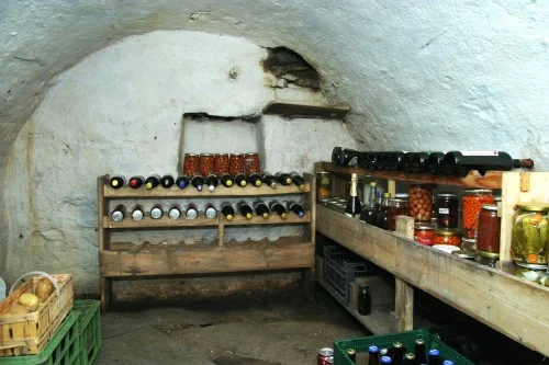 Podzemní sklep s dřevěnými regály pro uložení lahví vína a konzerv.