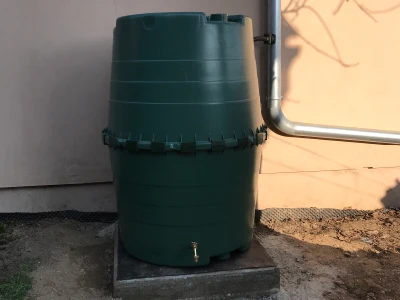 Zelená nádrž na dešťovou vodu stojící venku u domu.