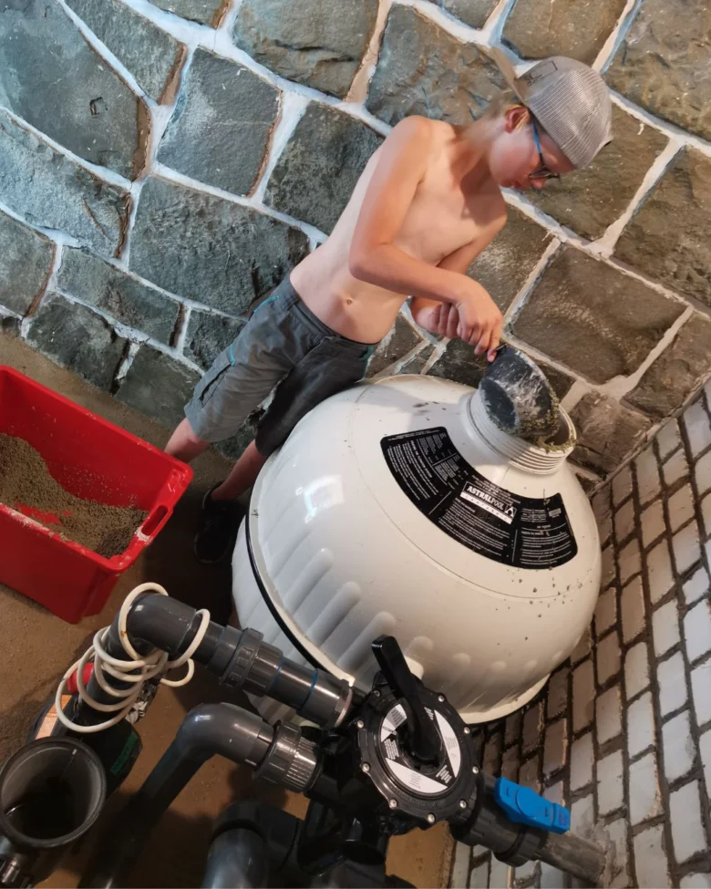 Chlapec nalévá písek do bazénové filtrace.