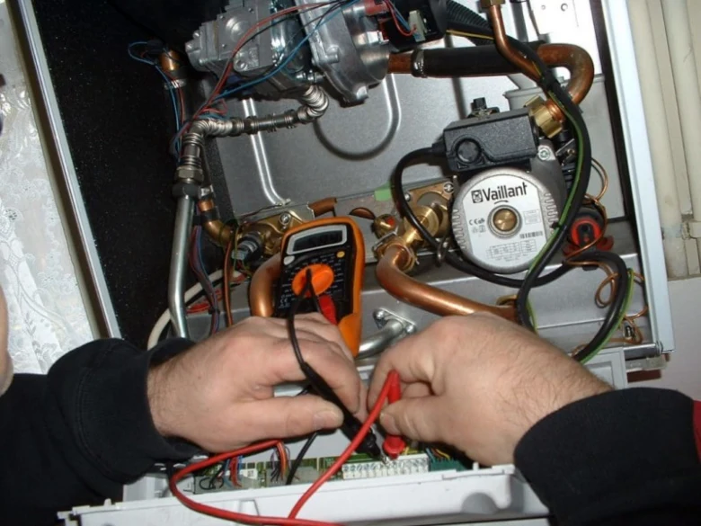 Ruční kontrola elektrických spojů v plynovém kotli multimetrem.