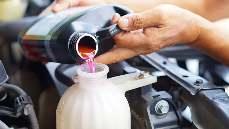 Nalévání růžové nemrznoucí směsi do rozšířovací nádrže motoru.
