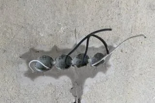Odkryté elektrické kabely v betonu panelového domu.