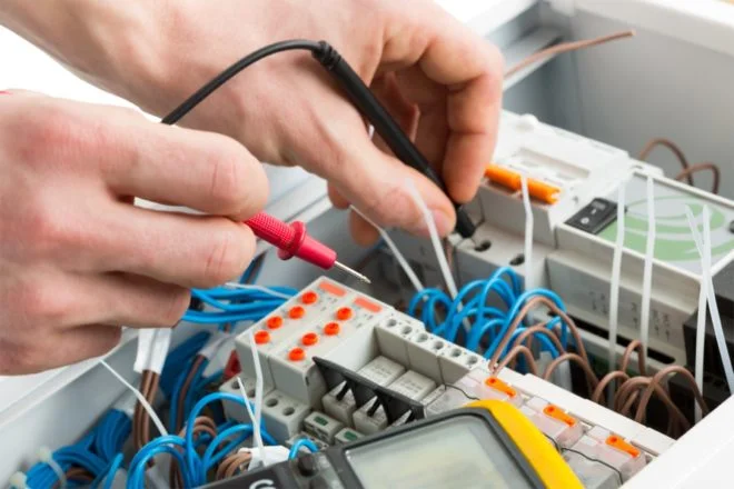 Elektrikář zkouší kabeláž v rozvaděči pomocí multimetru.