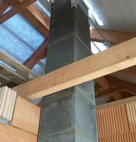 Kamenný komín s kovovými úchyty v dřevěné konstrukci střechy.