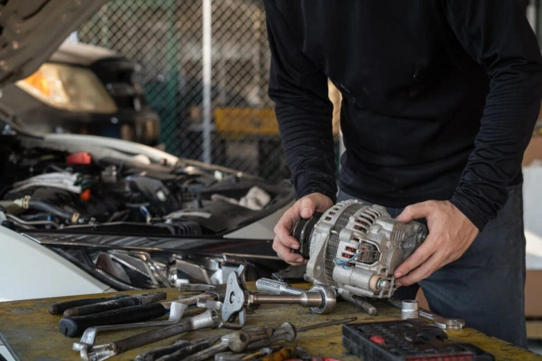 Mechanik drží střídač u auta s otevřenou motorkou.