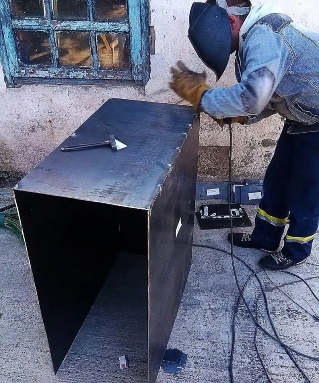 Svářeč staví kovovou krabici pro výrobu pyrolýzního kotlíku.