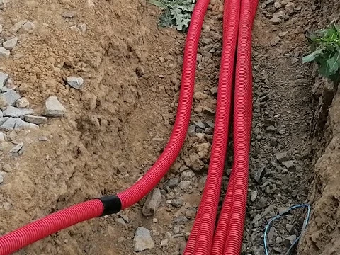 Červené plastové kabelovody v zemi pro chatu