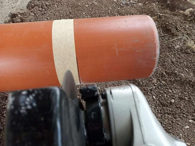 Oranžová plastová trubka se řezá pilou v zemi.