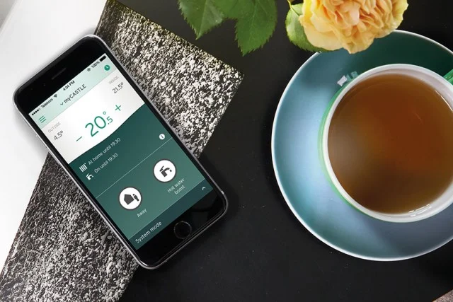 Smartfon s aplikací pro domácnost vedle šálku čaje.