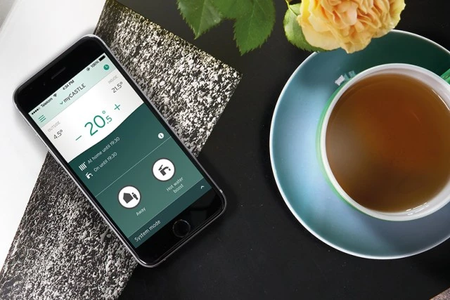 Smartfon s aplikací pro řízení kotla vedle šálku čaje.