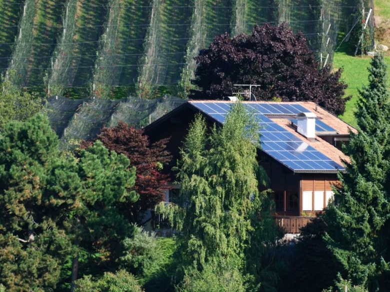 Dům s fotovoltaickými panely na střeše v krajině.