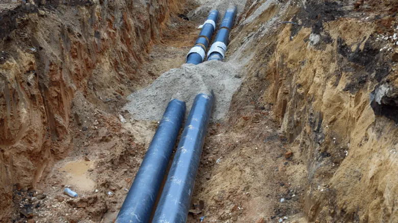 Modrá vodovodní potrubí v vykopaném příkopu pro instalaci.