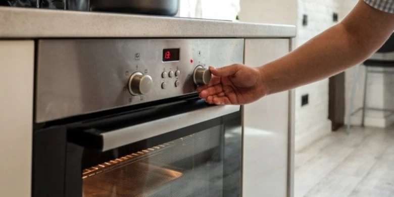 Ruka otáčí knoflík na troubě v kuchyni.
