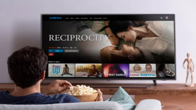 Muž sedí před televizorem s popcornem - typický domácí zábavní scénář.