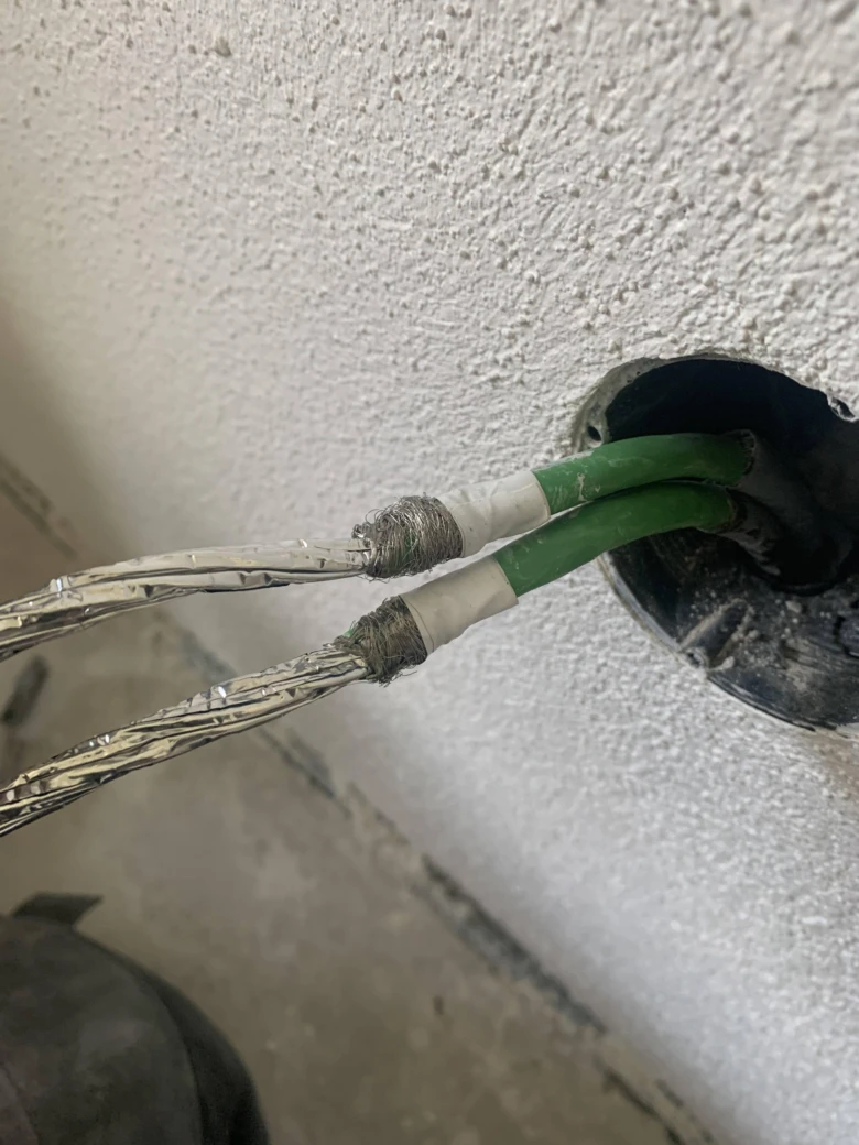Zelené elektrické kabely s odhalenými vodiči vyčnívajícími ze zdi.