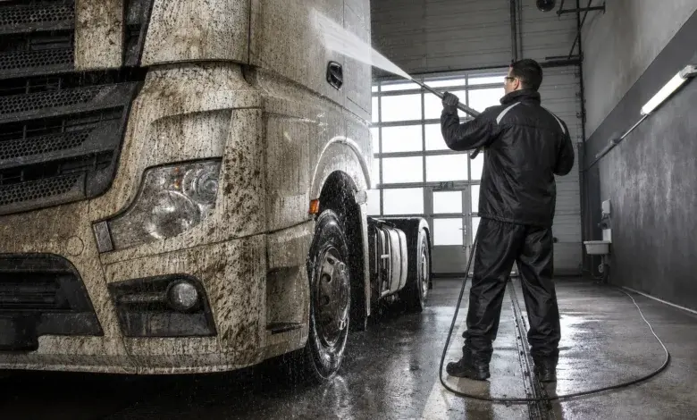 Muž myje velkou nákladní automobil vysokotlakou vodou v garáži.