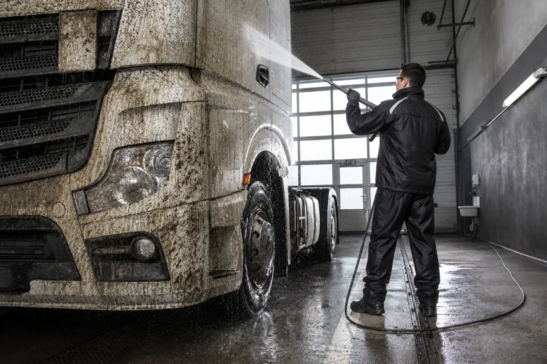Muž myje velkou nákladní automobil vysokotlakou vodou v garáži.