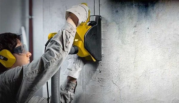 Pracovník řezá drážku do zdi pro elektroinstalaci