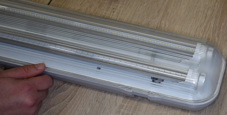 Ruka drží rozloženou bílou LED zářivku s viditelnými vnitřními komponenty.