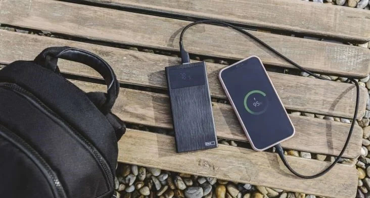 Smartfon nabíjený externím akumulátorem na dřevěné desce.