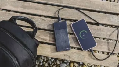 Nabíjecí banka dobíjí telefon na dřevěné lavičce vedle batohu.