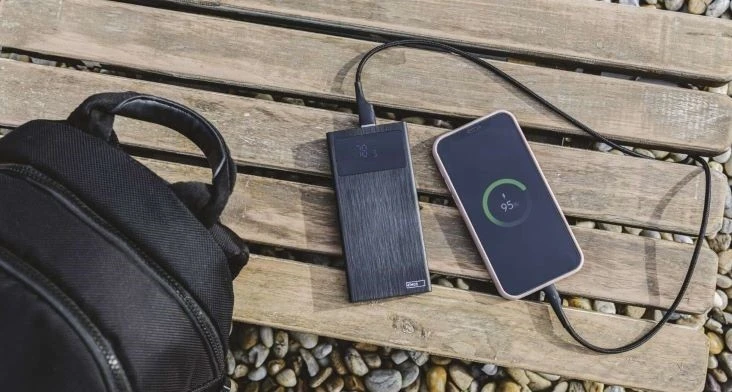 Nabíjecí banka dobíjí telefon na dřevěné lavičce vedle batohu.