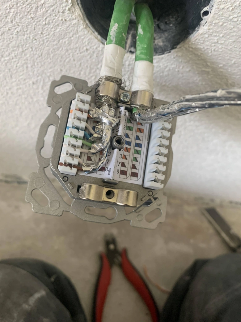 Otevřená elektrická zásuvka s viditelnými vodiči a nástroji pro kontrolu připojení.