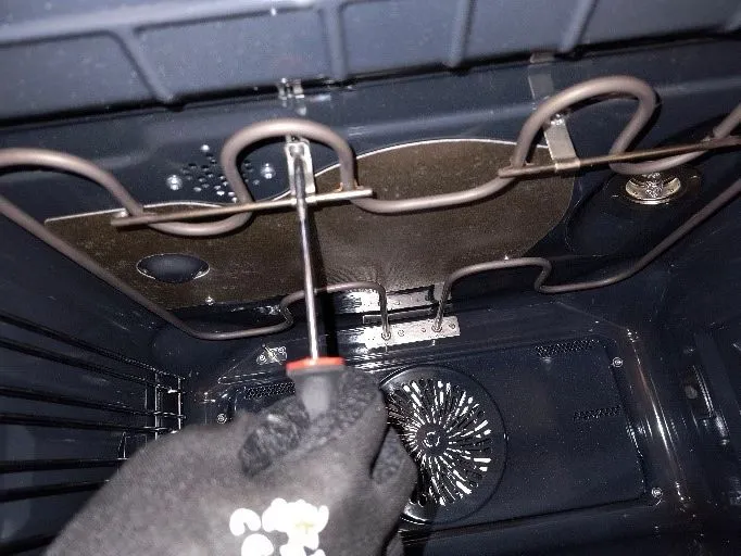 Ručník s šroubovákem odšrouvává horní ohřívač v elektrické troubě.