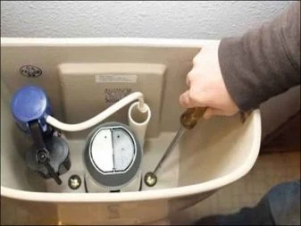 Ruční úprava plováku v nádržce toalety šroubovákem.
