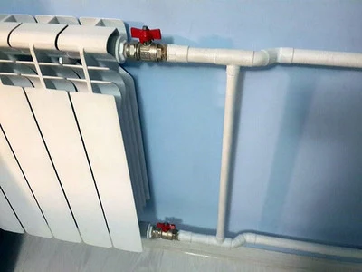 Bílý radiátor s přívodním i zpátečním potrubím v topení.