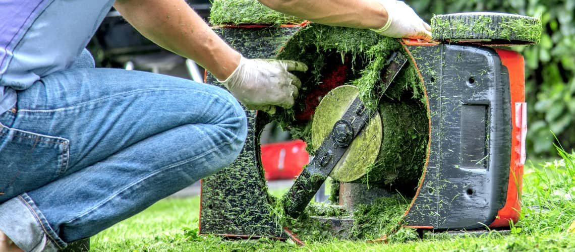 Člověk čistí trávu z elektrické sekačky pro opravu.