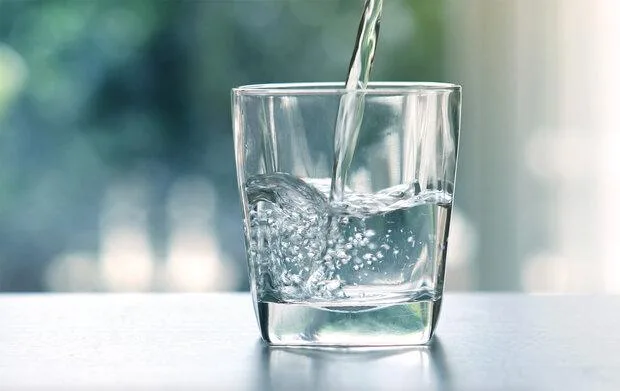 Voda se nalévá do sklenice na stolu.