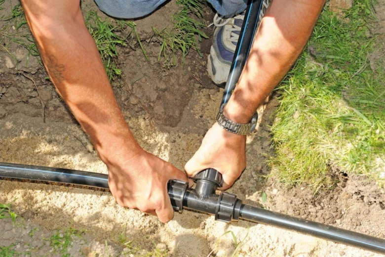 Ruční připojení černých plastových trubek v zemi pro instalaci.
