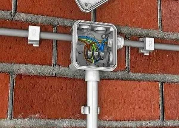 Otevřená elektrická spojovací krabice s viditelnými kabely na cihlové zdi.