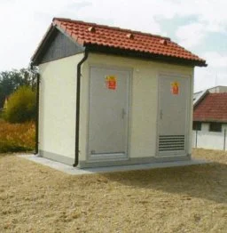 Malá trafostanice s červenou střechou na suché trávě.