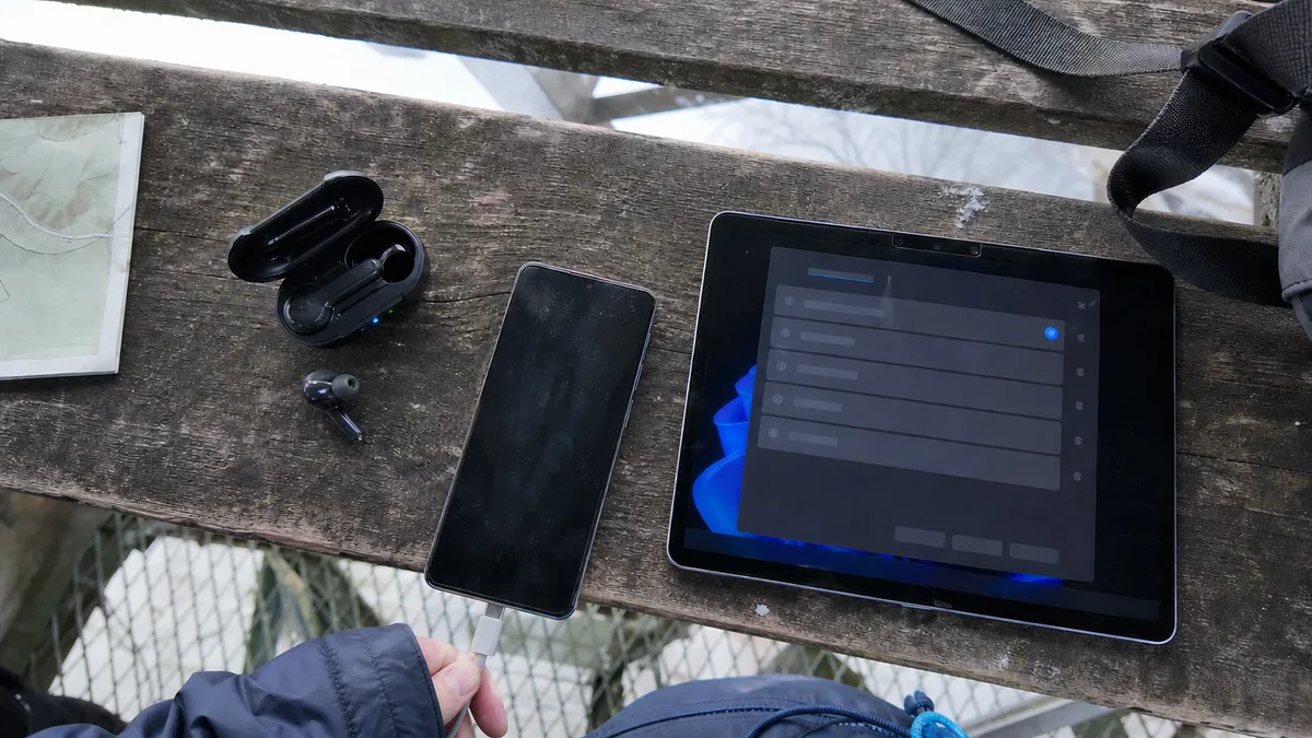 Tablet s mobilním telefonem a bezdrátovými sluchátky na dřevěné lavičce.