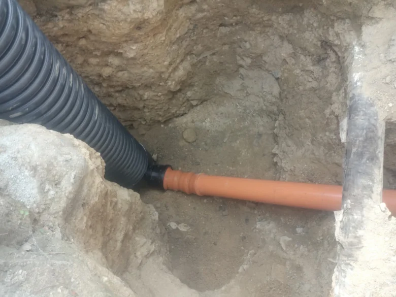 PVC kanalizační trubka v zemi s propojenou černou trubicí.
