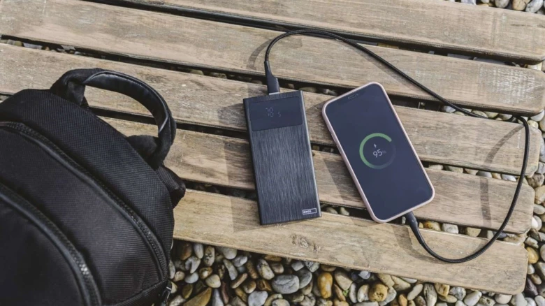 Powerbank nabíjí telefon na dřevěné lavičce vedle batohu.