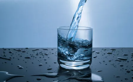 Voda se nalévá do sklenice na tmavém povrchu.