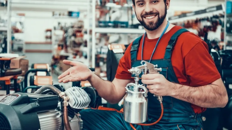 Mechanik s pistovým kompresorem a sprejovou pistolí v dílně.