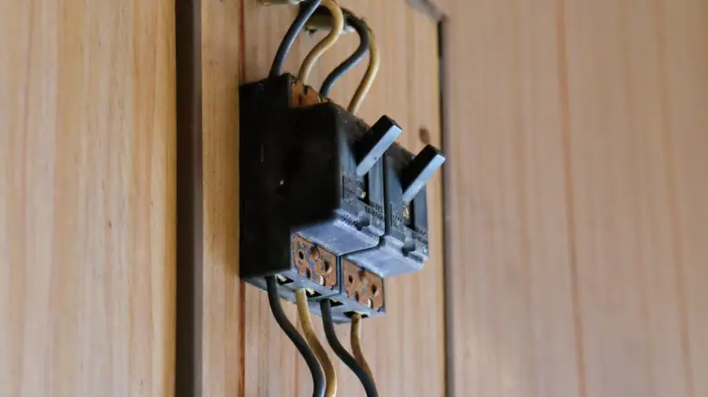 Černý elektrický přepínač s propojenými vodiči na dřevěné desce.