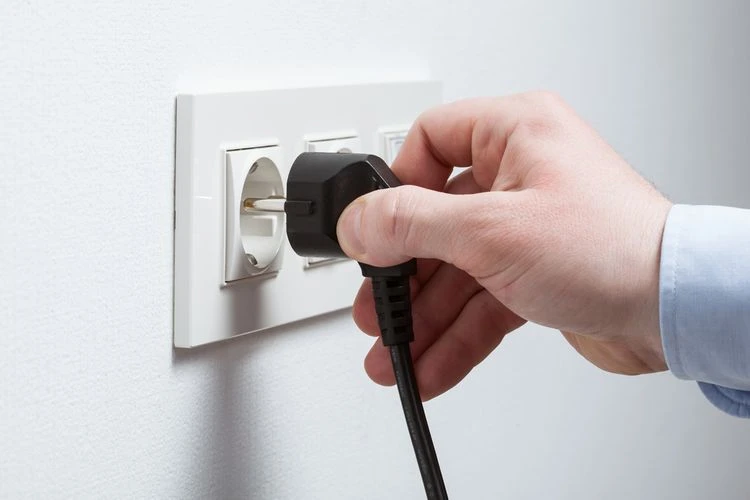 Ruka zapojuje černý evropský elektrický konektor do bílé zásuvky na stěně.