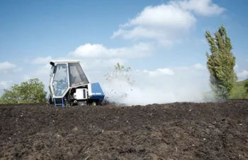 Traktor pěstuje půdu na poli pod modrou oblohou.