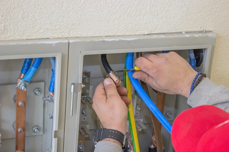 Elektrikář připojuje vodiče v rozvaděči pro zemnicí systém.