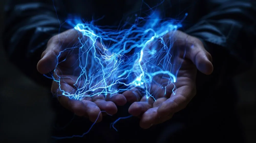 Ruce drží modré elektrické výboje v temnotě.