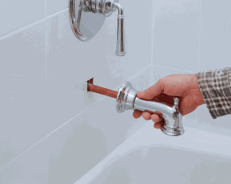 Instalace koupelnové baterie do zdi s viditelným měděným potrubím.
