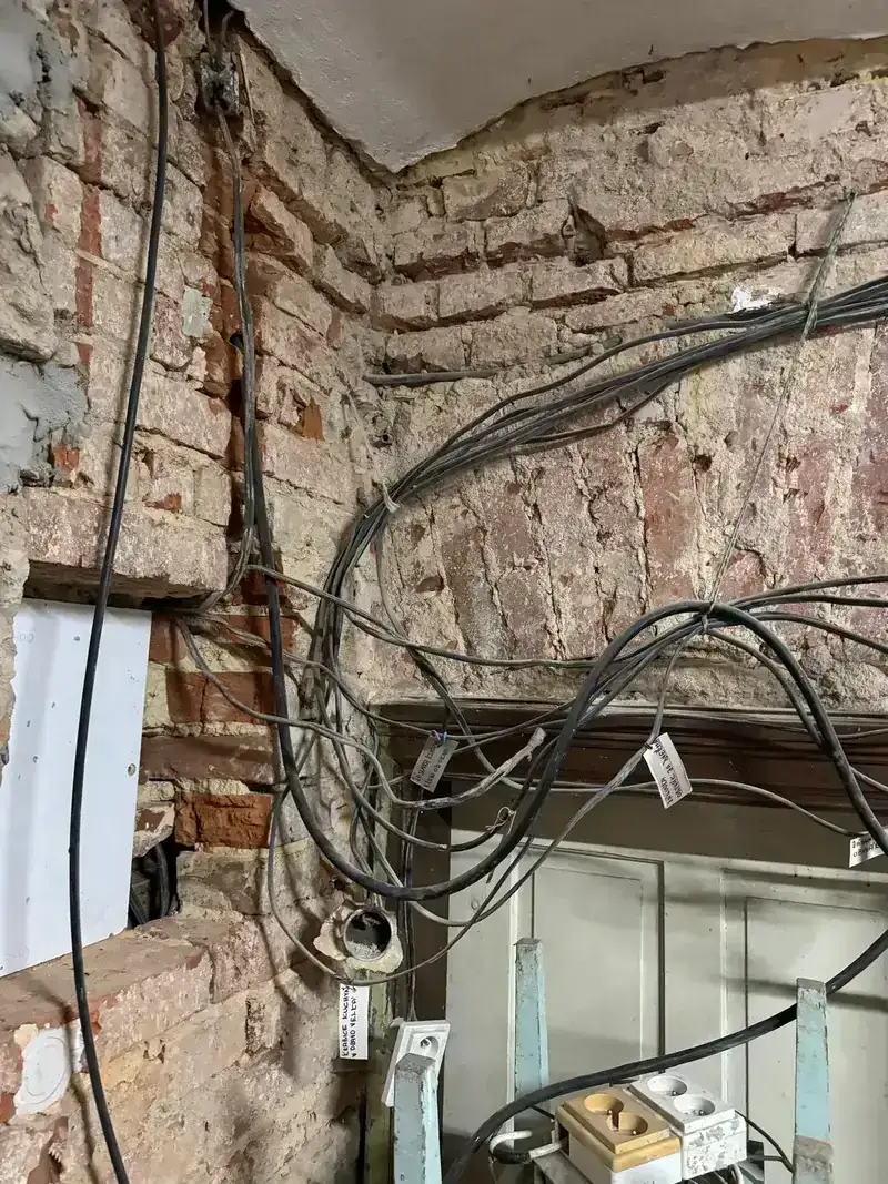Zamotané staré elektrické kabely v nehotové cihlové stěně s viditelnými poškozeními.