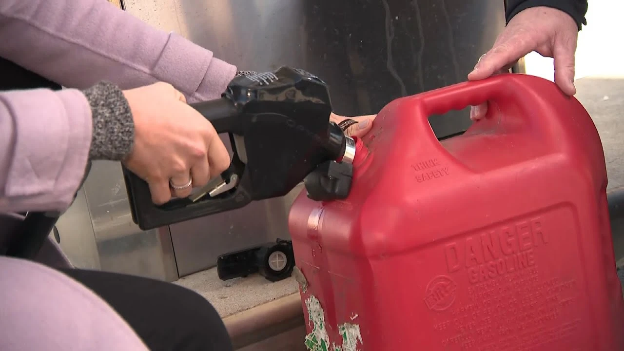Lid naplňuje červenou plastovou nádobu s benzínem na čerpací stanici.