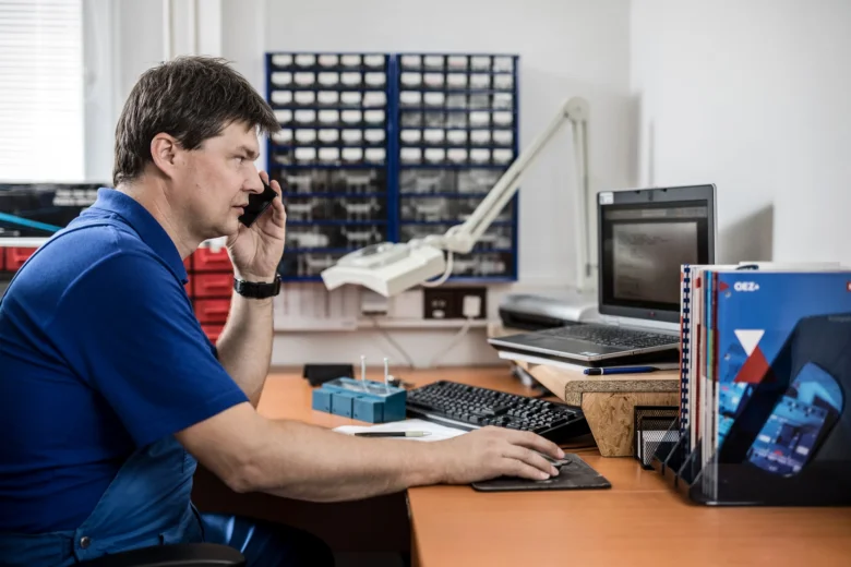 Elektrikář pracuje u počítače v kanceláři s technickým vybavením.